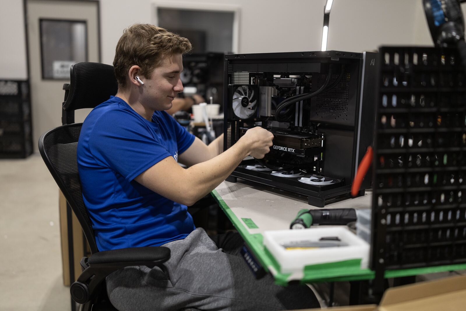 A technician assembling a GPU workstation at a bench, components laid out in trays beside them.