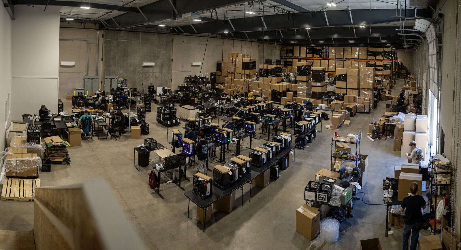 Rows of benches on the build floor with GPU workstations under assembly and pallets of components against the far wall.