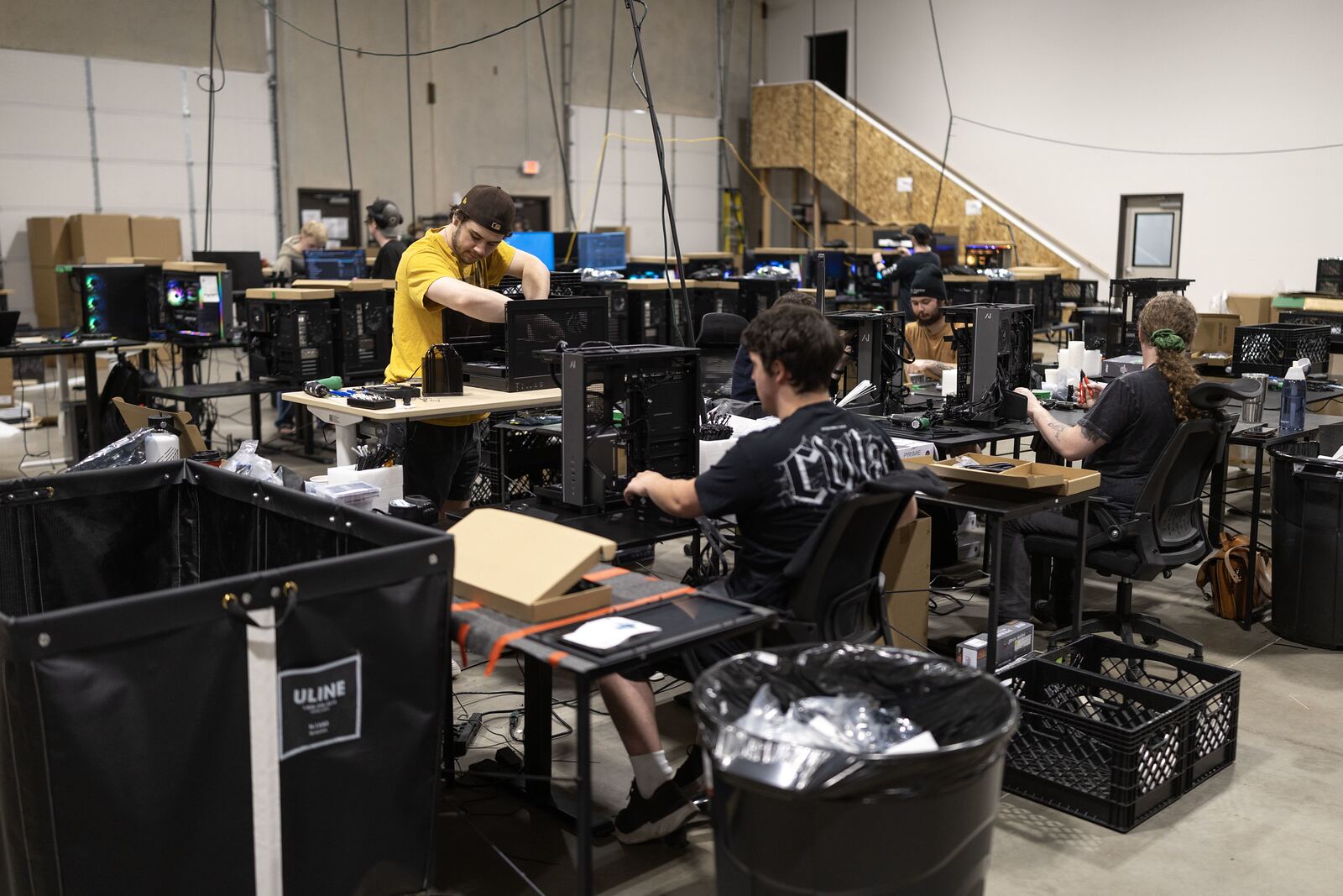 Wide view of the build floor with technicians at standing benches and machines under test.