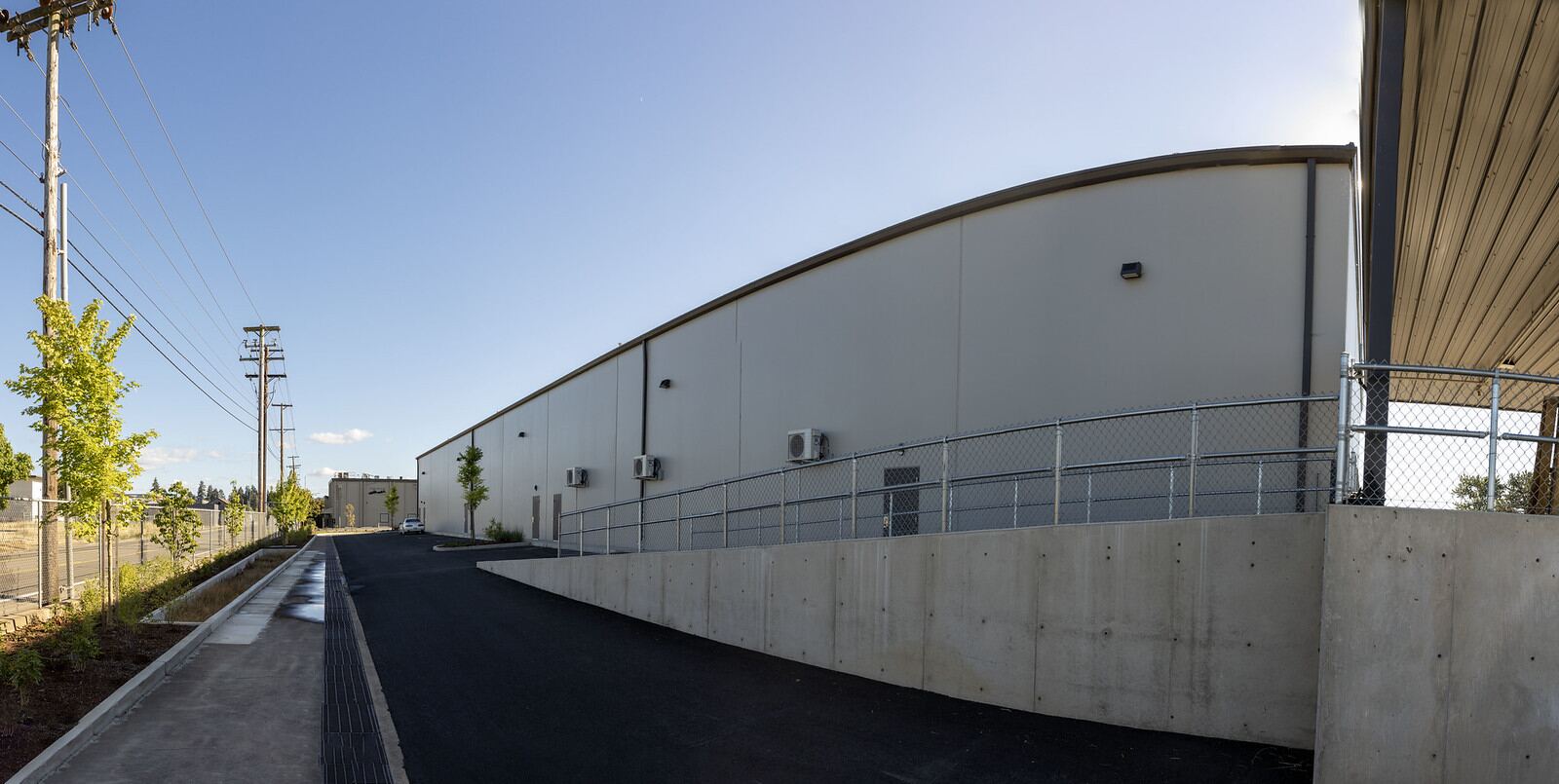 The long east wall of 80 N Danebo Avenue seen from the access road, with the power line running alongside.