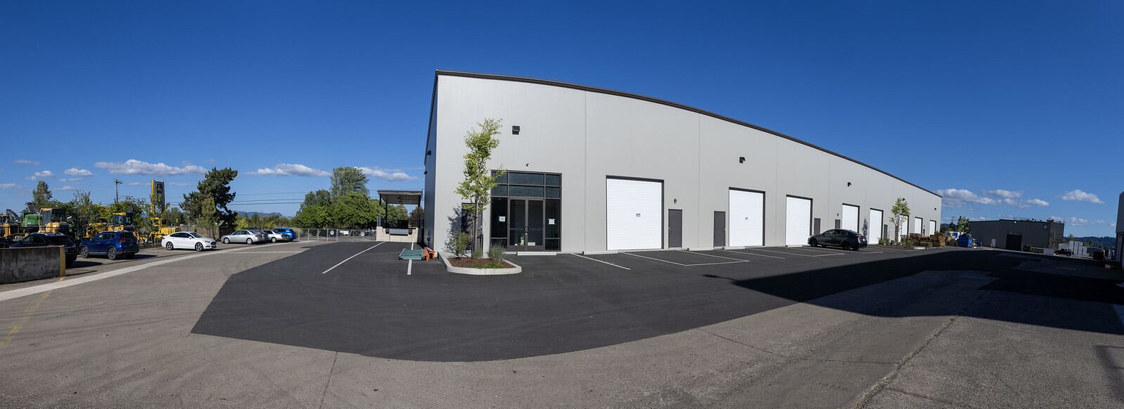 The building at 80 N Danebo Avenue, Eugene, Oregon: a long single-storey concrete tilt-up with white roll-up bay doors and a freshly resurfaced lot under a clear sky.
