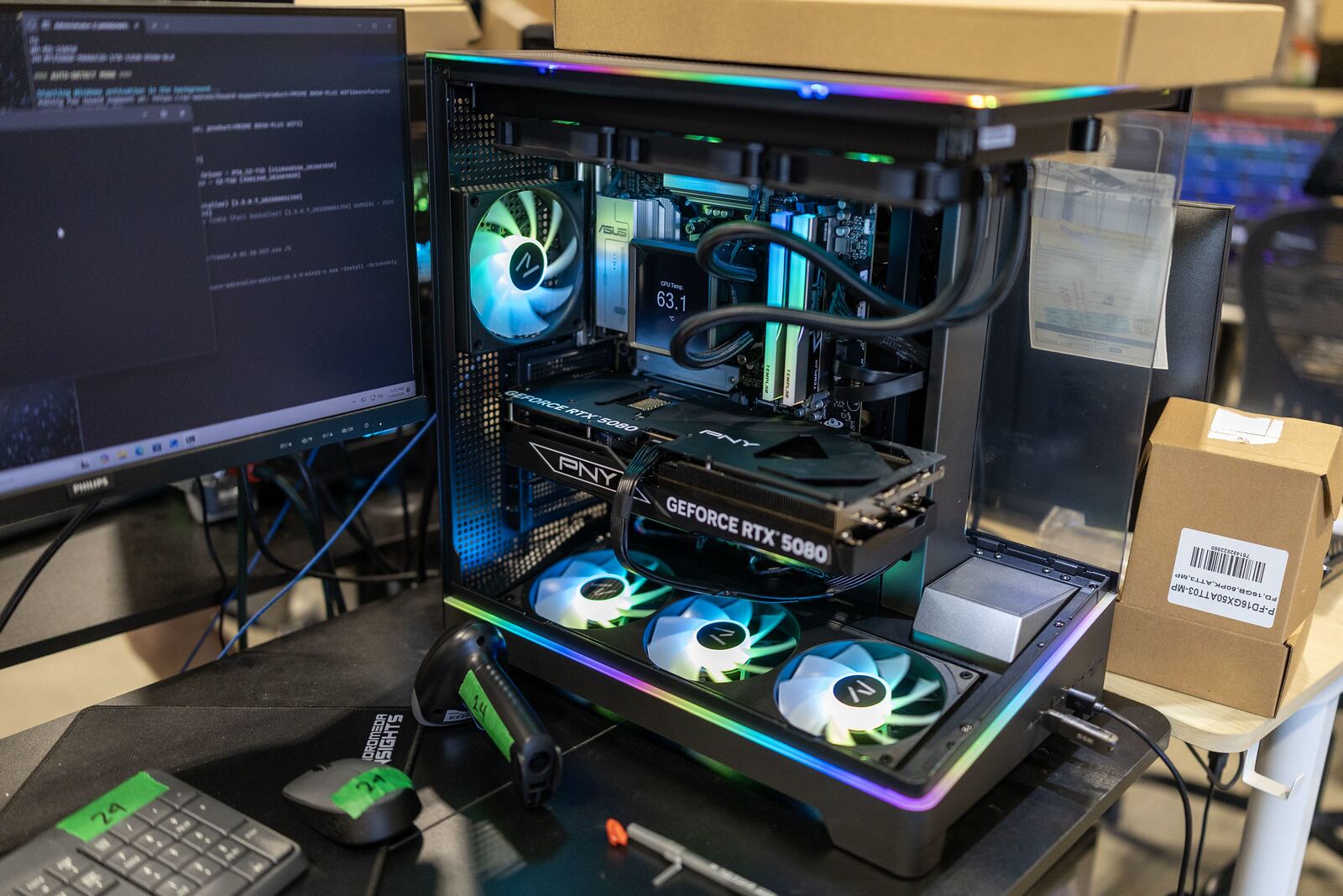 A GPU workstation open on a bench beside monitors showing a running job.